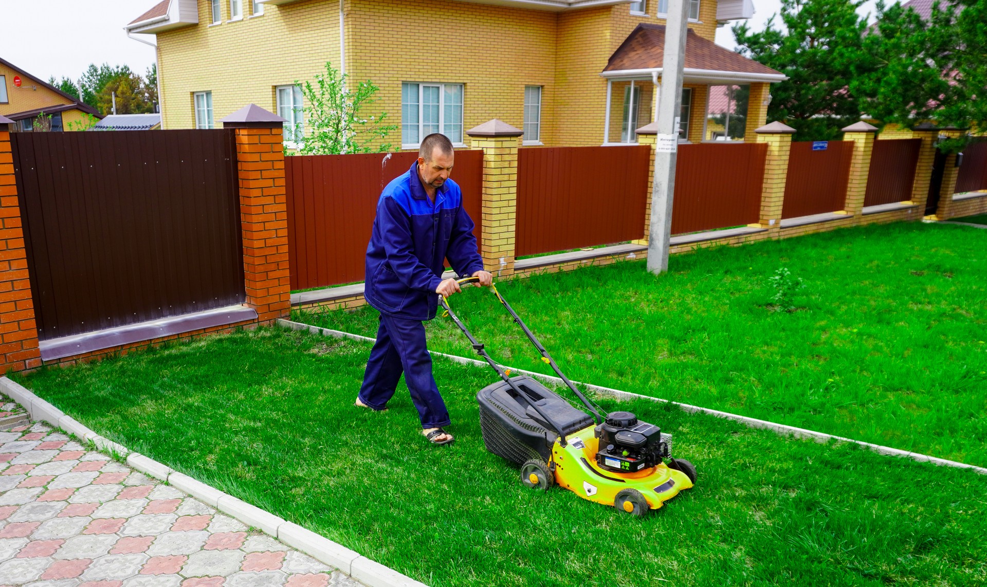 The man is working in the garden. Mowing grass with a lawn mower.